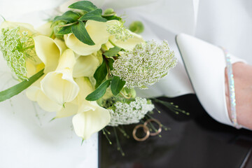 Bride resting her legs in elegant white heels near a window, with a wedding bouquet on a black table. Soft natural light, calm morning atmosphere, bridal preparation concept