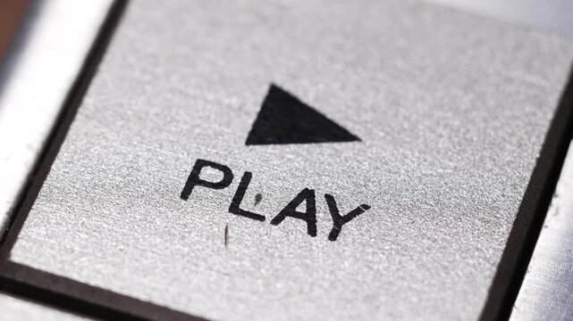 Macro close up of finger pressing silver play button with black triangle icon