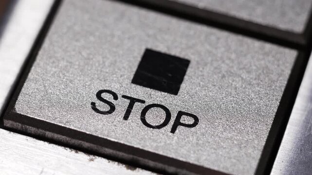 Macro close up of finger pressing silver stop button with black square icon