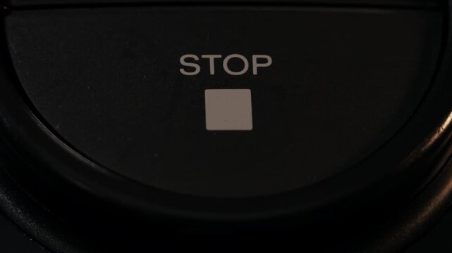 Close up finger pressing circular stop button with square icon in dark setting