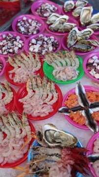 Vertical screen colorful plates packed with fresh shrimp octopus pieces and oysters sit on ice creating a vibrant italian seafood market moment with raw textures and coastal food energy