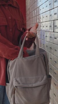 vertical shot. A woman opens her mailbox and takes out her mail. Mail delivery concept.