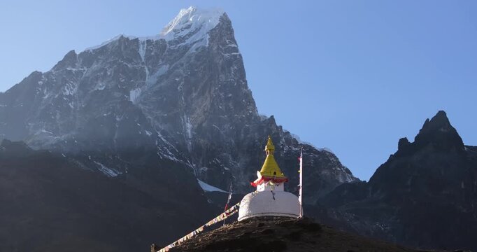 Orbiting aerial drone shot with parallax of a white Buddhist stupa in Dingboche, Nepal. Prayer flags flutter against the Himalayan mountain landscape in the Everest region.