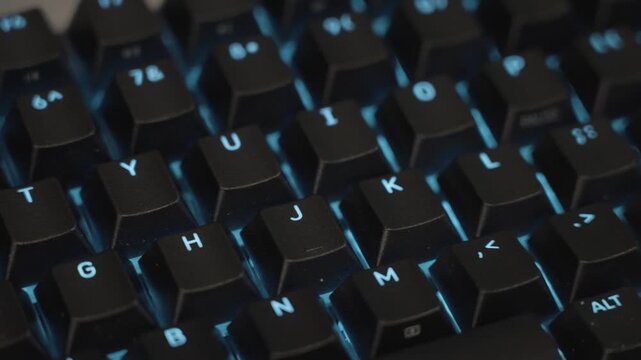 RGB lights in blue shade shining through black keycaps on a modern mechanical keyboard.