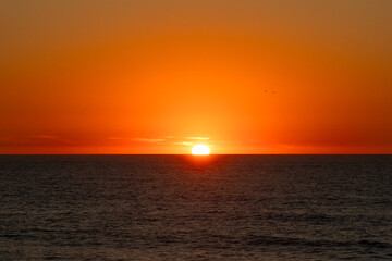 Obraz premium Fiery sun sinking below the ocean horizon during an intense orange sunset, Portugal, Ovar – Furadouro, 10.10.2025