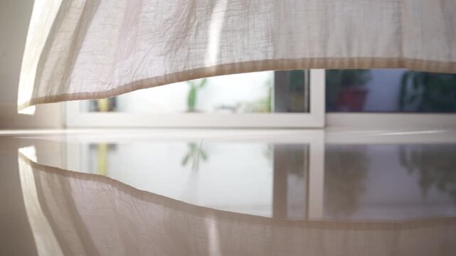 Blowing sheer white curtains by large glass door with warm morning sunlight and blurry garden trees view in white room