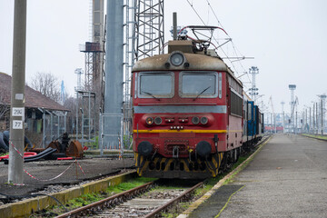 a station platform shows a vintage red electric locomotive pulling a train 