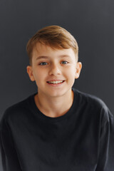 Young boy smiles at camera while standing against a dark background © andrey