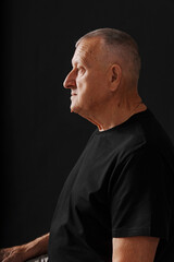 Fototapeta premium Elderly man sitting against dark background looks deep in thought
