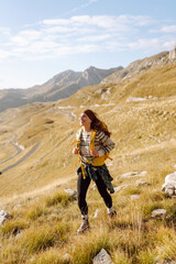 A happy hiker with a yellow backpack enjoys the mountain scenery on a hiking trail. The young woman feels the freedom of the outdoors. Concept of hiking, freedom, and adventure. © maxbelchenko