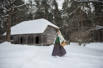Latvian woman in traditional dress poses in a village in winter. Riga, Latvia.