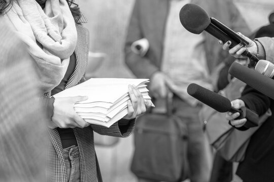 Female whistleblower holding documents speaks at press conference to journalists with microphones, exposing corruption, transparency, public interest, media coverage and investigative journalism