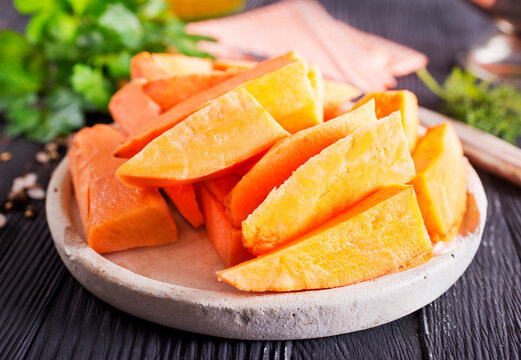 Fresh raw sweet potatoes, with fresh greens and salt on gray table