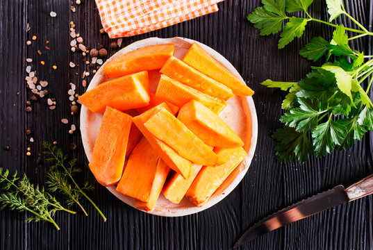 Fresh raw sweet potatoes, with fresh greens and salt on gray table