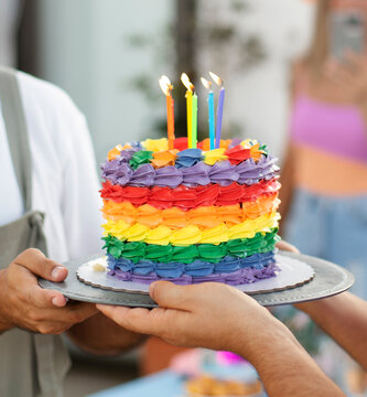 Couple celebrating with a vibrant rainbow layer cake and lit candles in a closeup shot