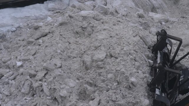 A detailed view of the process of grabbing compacted snow with a powerful loader bucket. Work on clearing the territory of blockages after extreme winter precipitation