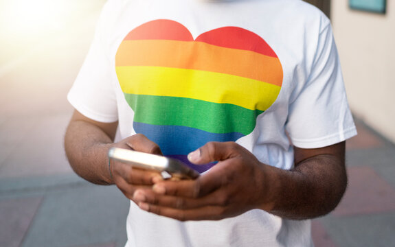 Individual in rainbow heart tshirt commemorating pride month while using a smartphone