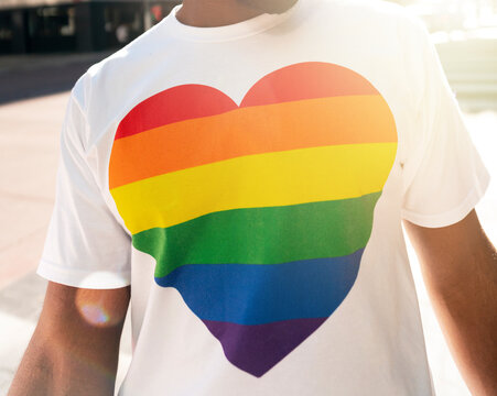 Person wearing a white tshirt with a rainbow heart design in a closeup shot at a pride month event
