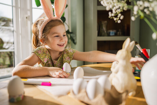 Child with bunny ears coloring Easter eggs at home in spring