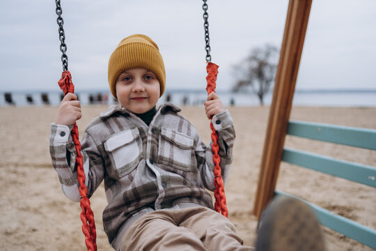 Child in yellow beanie on swing at beach smiling outdoors