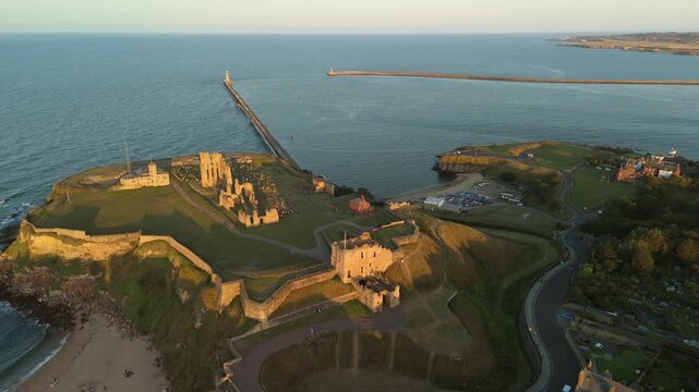 Sunset casts a warm glow over Tynemouth Pier along the North Sea at dusk. Aerial drone footage