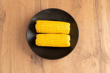 Boiled corn on black plate on wooden background for healthy food  