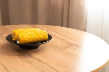 Boiled corn on a black plate resting on a wooden table indoors  