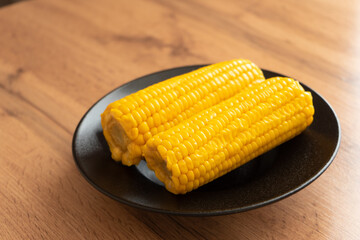 Boiled sweet corn on a black plate on wooden table  