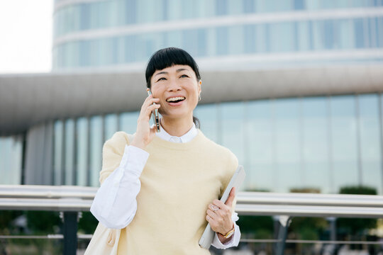 Smiling woman using mobile phone in casual outfit outdoors in business district