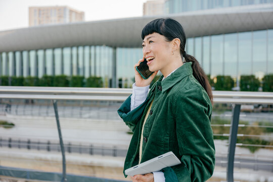 Confident businesswoman talking on mobile phone outdoors holding tablet
