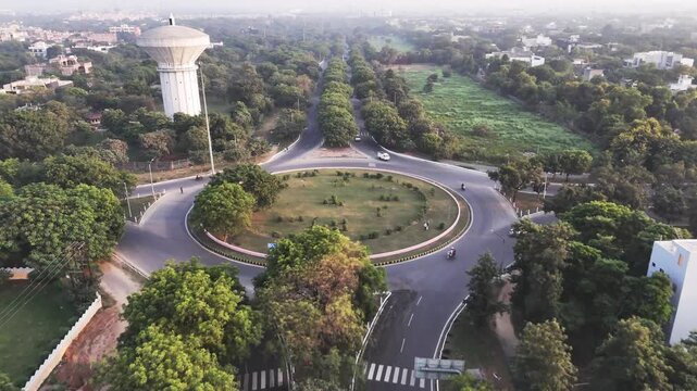 Aerial video of a landscaped roundabout in Greater Noida, where tree-lined roads intersect around a circular green island, highlighting planned infrastructure and smooth urban traffic flow.