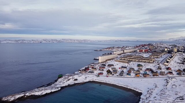 Scenic aerial panorama of Nuuk, Greenland, featuring colorful Nordic houses in a snow-covered landscape, modern city architecture, and the Arctic ocean under a sunset sky.