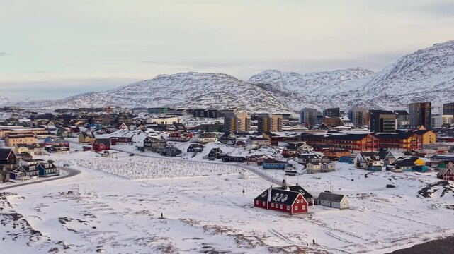 Scenic aerial panorama of Nuuk, Greenland. Featuring iconic colorful Nordic houses, snow-covered streets, and the historic colonial harbor against a backdrop of majestic Arctic mountains.