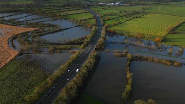 Drone view of Malton bypass A64 dual carraigeway with cars driving runs over a flooded River Derwent and surrounding green fields on sunny winter day