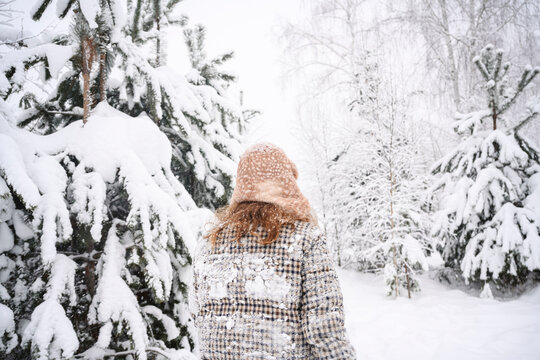 Back view of person in warm hat walking outdoors in snowy winter forest