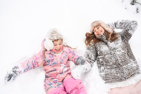 Mother and daughter laughing together in snow wearing winter clothing
