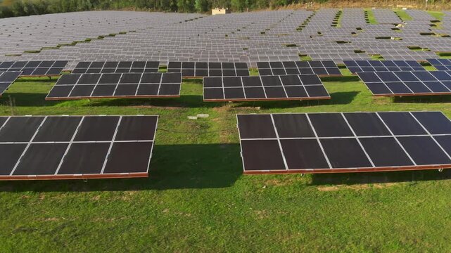 Aerial dolly left over expansive solar panel farm on lush green hillside in rural countryside.
