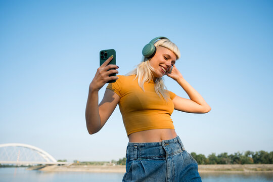 Woman dancing outdoors with headphones and smartphone on sunny day