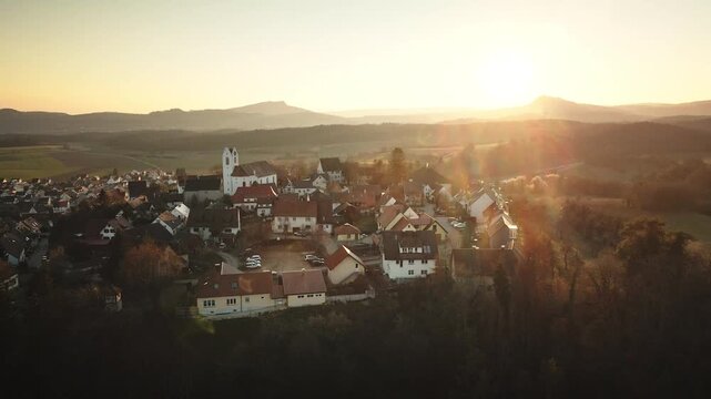 Lateral drone move to the right over Aach&rsquo;s old town at sunset, passing rooftops and the church tower as warm golden light and distant hills frame the village panorama.