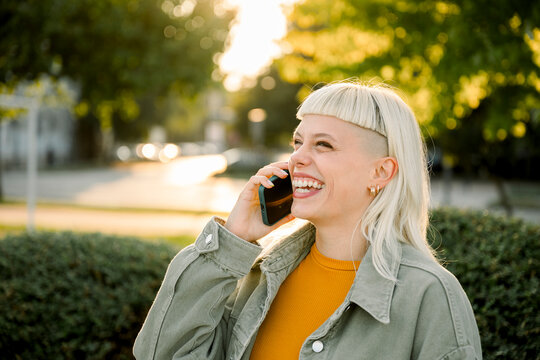 Laughing woman making phone call outdoors in city wearing casual clothes