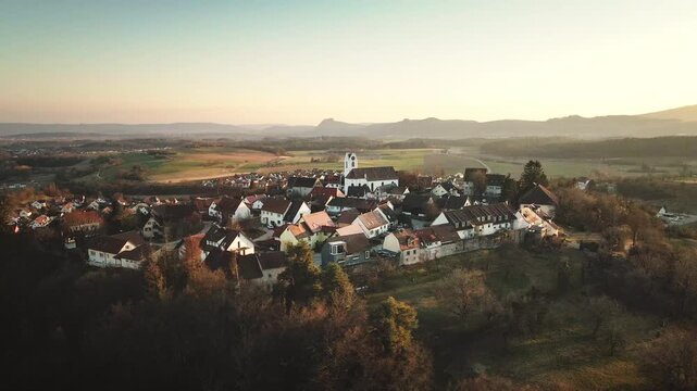 Lateral drone move to the right over Aach&rsquo;s old town at sunset, passing rooftops and the church tower as warm golden light and distant hills frame the village panorama.