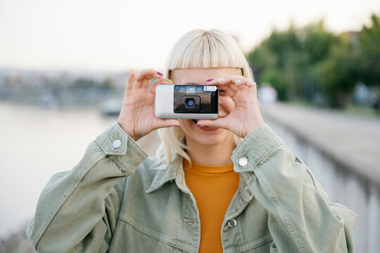 Hipster with retro camera taking photo outdoors in casual clothing