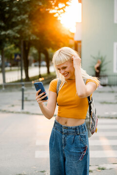 Smiling woman in casual wear using mobile phone outdoors at sunset