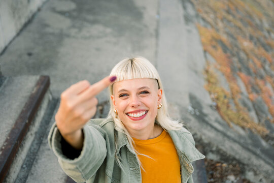 Smiling woman sitting outdoors making gesture and looking at camera