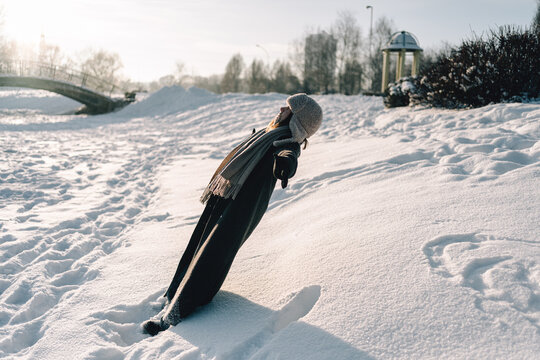 Young woman in winter clothing leaning back falling into snow on sunny day