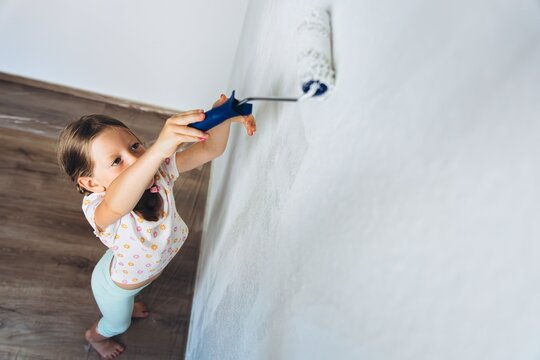 Child painting wall with roller during home renovation indoors