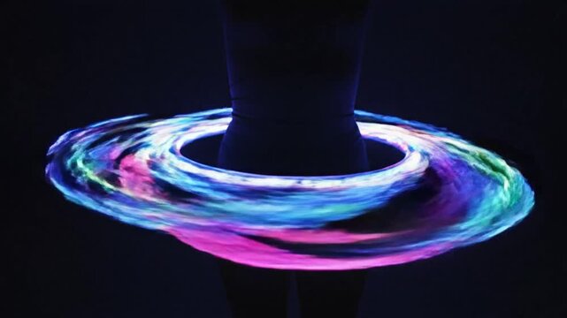 A person spinning a glowing hula hoop around their waist in a dark room