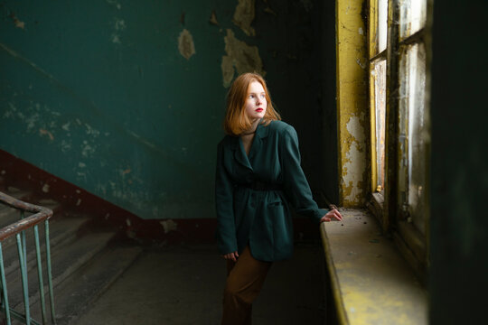 Teenager with red hair in green jacket standing by window in old entrance