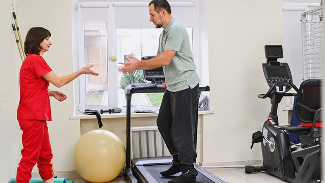 A man recovers from an injury on a treadmill under the guidance of a physical therapist. Stroke rehabilitation, physical activity. Restoration of brain functions and motor coordination