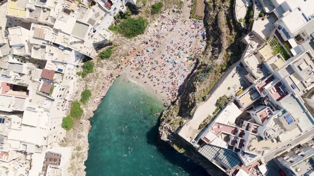 Aerial view of Lama Monachile beach with its turquoise waters, framed by towering cliffs and quaint white buildings, Polignano a Mare, Apulia, Italy.